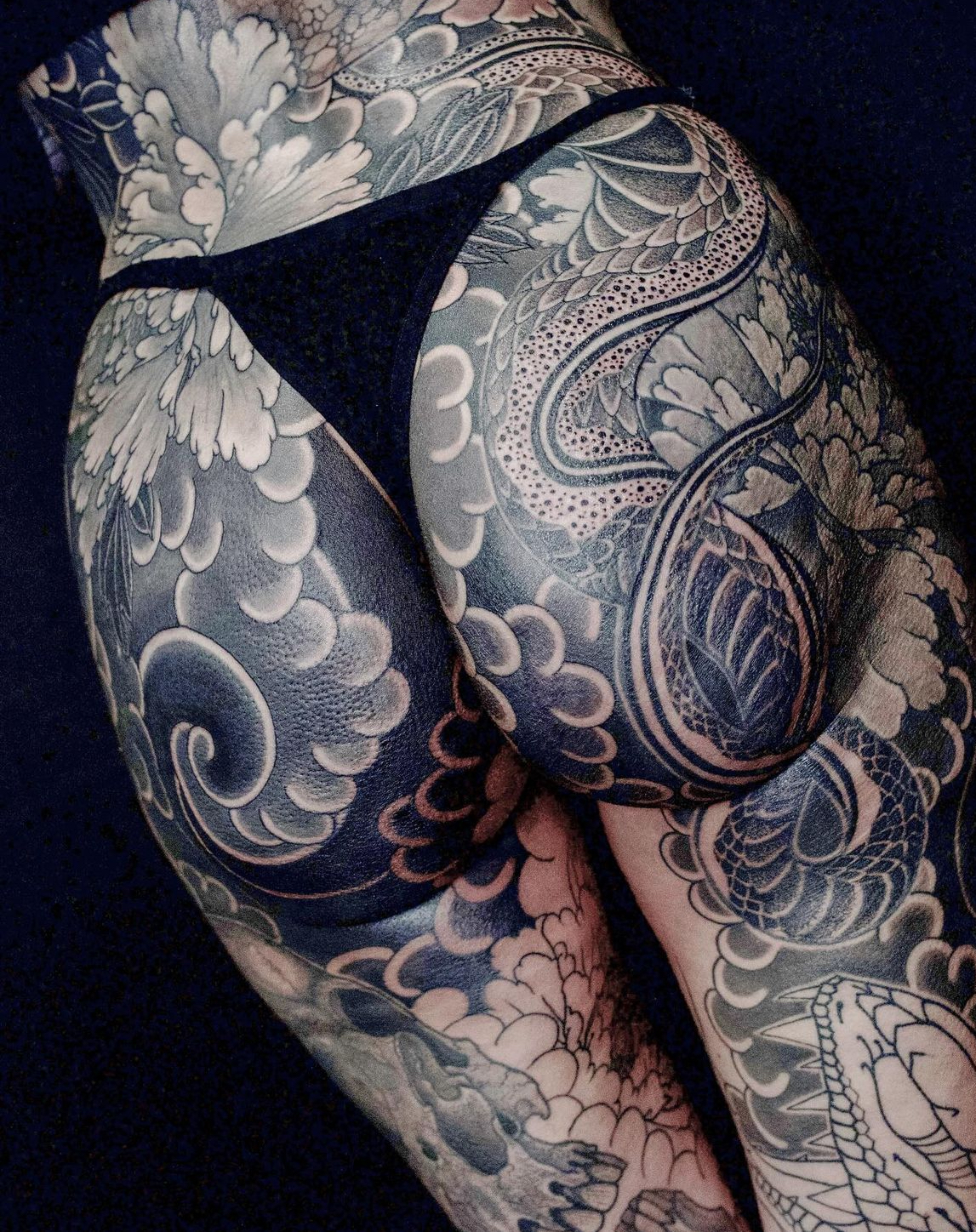 photo of tattoo with black and grey snakes, peonies, and skulls on a woman in black and grey.